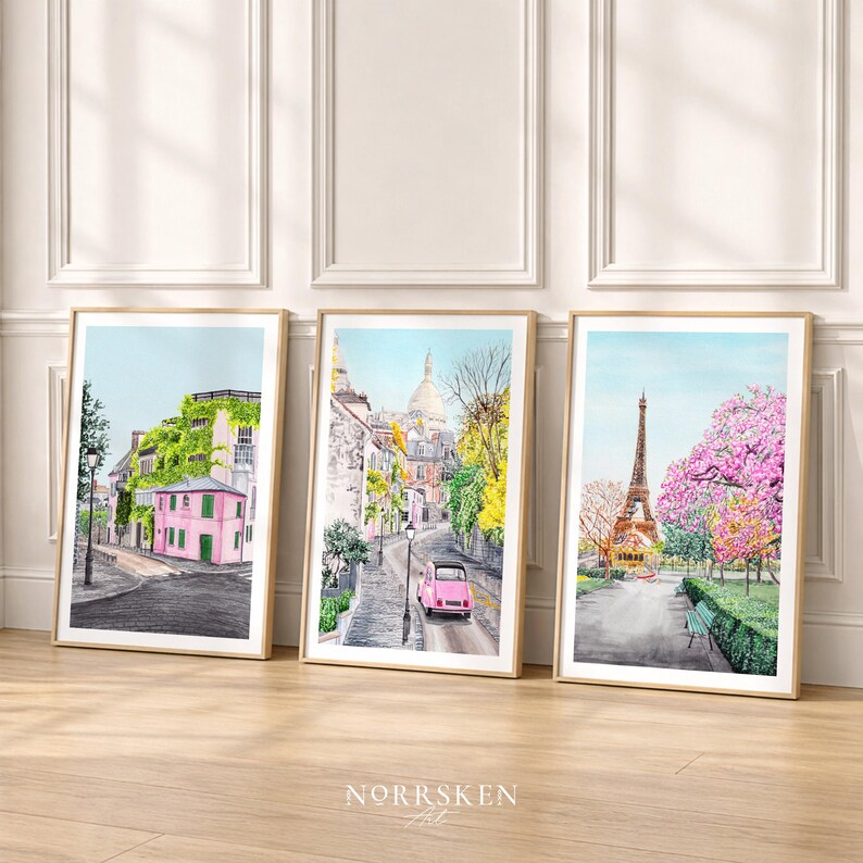 May include: Three framed watercolor prints depicting Parisian street scenes. One features a pink building covered in ivy, another a pink car on a cobblestone street, and the last the Eiffel Tower with pink flowering trees.