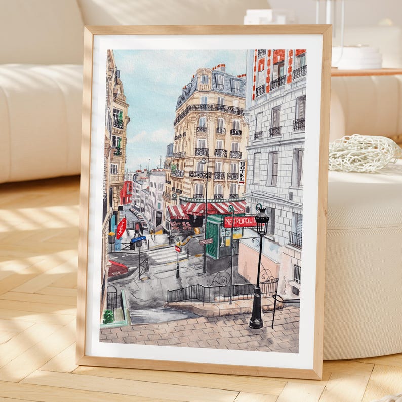 K&ouml;nnte beinhalten: Gerahmter Aquarelldruck einer Pariser Stra&szlig;enszene. Das Kunstwerk zeigt Geb&auml;ude, einen Zebrastreifen und eine Stra&szlig;enlaterne. Die Farbpalette umfasst Beige-, Rot- und Blaut&ouml;ne und schafft eine klassische europ&auml;ische &Auml;sthetik.