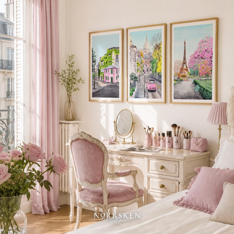 May include: Three framed watercolor prints depicting Parisian street scenes and the Eiffel Tower hang above a white vanity desk. The desk features a round mirror, makeup brushes, and a pink chair. The room includes pink curtains and roses.