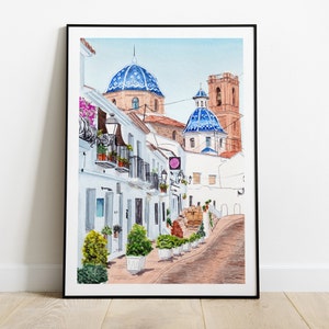 May include: Watercolor painting of a narrow street in a Spanish town. The street is lined with white buildings with blue tiled roofs. There are potted plants and trees along the street.