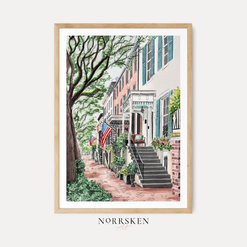 May include: A watercolor art print depicting a street scene with historic townhouses, a large tree, and American flags. The buildings feature light-colored facades, blue shutters, and brick steps leading to porches. The text NORRSKEN Art is at the bottom.