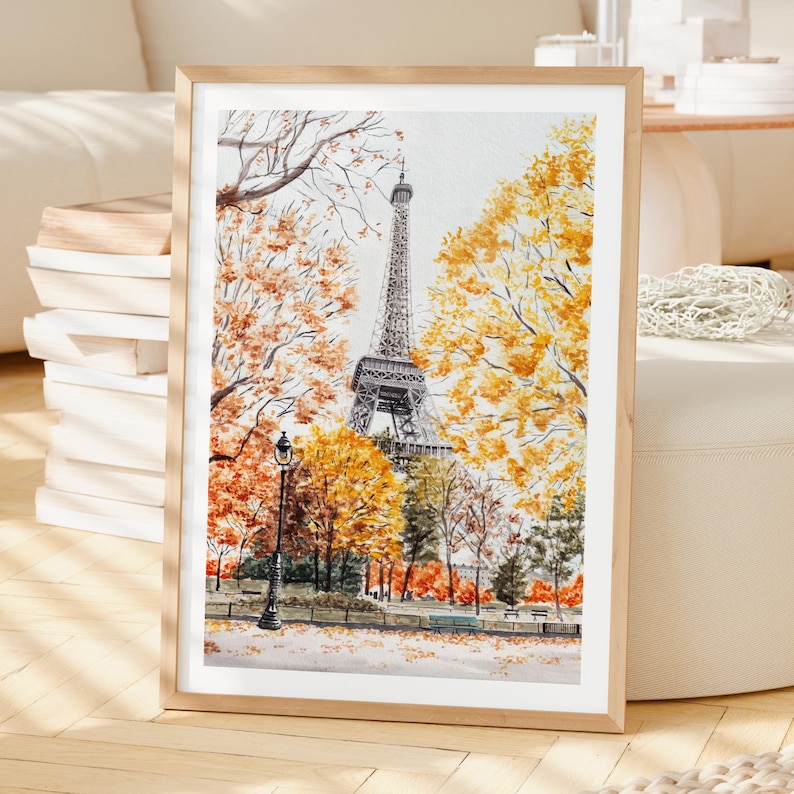 K&ouml;nnte beinhalten: Gerahmtes Aquarellgem&auml;lde des Eiffelturms in Paris. Das Kunstwerk zeigt den Turm umgeben von B&auml;umen mit herbstlichem Laub in Gelb-, Orange- und Rott&ouml;nen. Eine schwarze Stra&szlig;enlaterne befindet sich im Vordergrund, in einem hellen Holzrahmen.