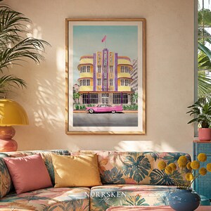 May include: A framed art print featuring a watercolor illustration of a yellow and purple Art Deco building with a pink vintage car parked in front. The building has a central tower with a pink flag on top and the text MARLIN visible on the facade.