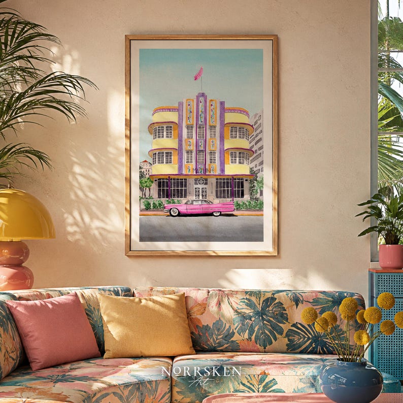May include: A framed art print featuring a watercolor illustration of a yellow and purple Art Deco building with a pink vintage car parked in front. The building has a central tower with a pink flag on top and the text MARLIN visible on the facade.