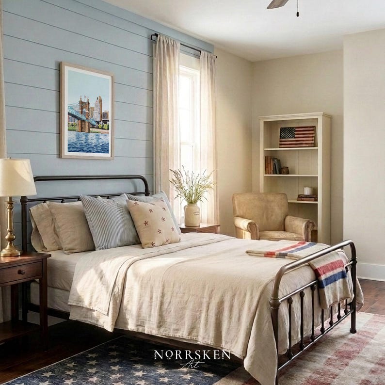May include: A bedroom with a black metal bed frame, beige bedding, and decorative pillows. A framed watercolor painting hangs on a blue wall. A nightstand with a lamp sits beside the bed. A rug with a star pattern is on the floor.