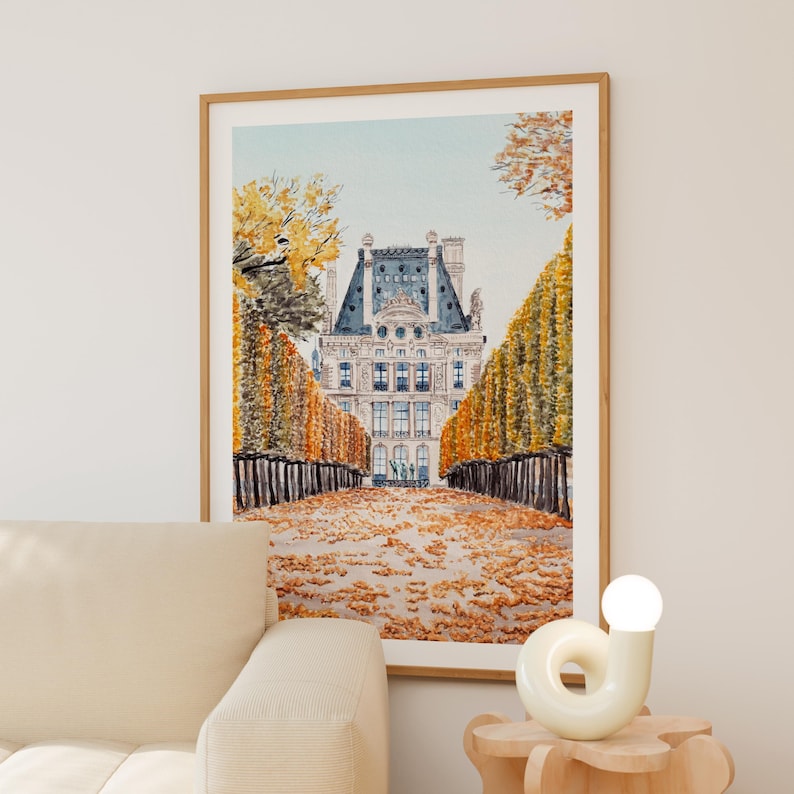 K&ouml;nnte beinhalten: Gerahmter Kunstdruck eines Geb&auml;udes mit blauem Dach. Das Kunstwerk zeigt einen Weg, der von goldenen B&auml;umen und Hecken ges&auml;umt ist. Der Boden ist mit Herbstlaub bedeckt und erzeugt eine herbstliche Szene.