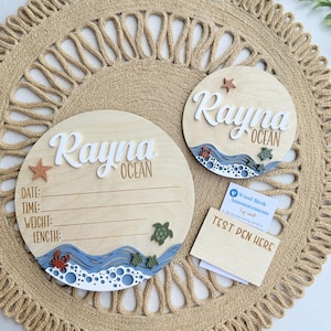 May include: Two circular wooden signs featuring the name Rayna Ocean in white and brown lettering. The larger sign includes lines for date, time, weight, and length. Both feature blue wave cutouts, a red crab, sea turtles, and a starfish.