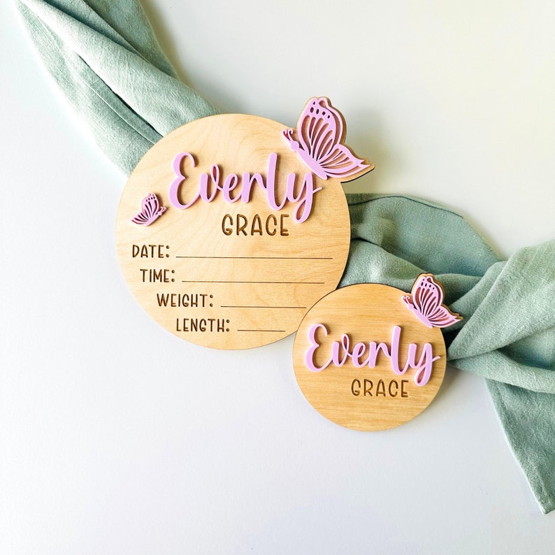May include: Two wooden baby name plaques featuring the name "Everly Grace" and pink butterfly embellishments. The larger plaque has sections to record the baby's date, time, weight, and length.
