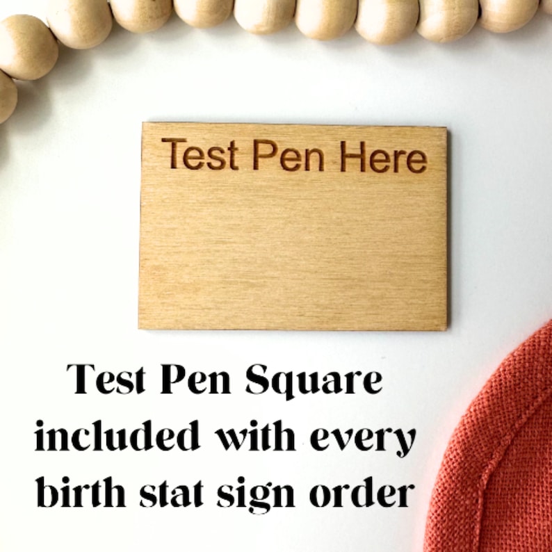 May include: A wooden square with the text "Test Pen Here" engraved on it. The square is light brown and has a smooth surface. Test Pen Square included with every birth stat sign order.