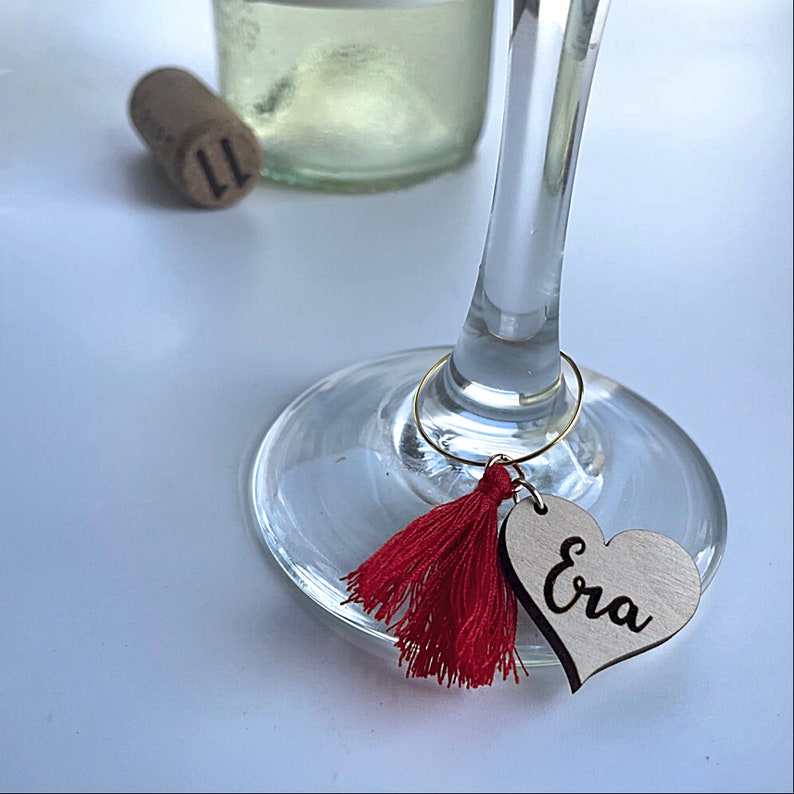 May include: A wine glass charm with a red tassel and a wooden heart tag that says "Era".