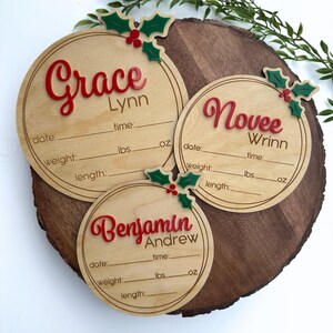 May include: Three round wooden ornaments with holly and berry accents. Each ornament has a name, "Grace Lynn", "Novee Wrinn", and "Benjamin Andrew", with spaces for date, time, weight in pounds and ounces, and length.