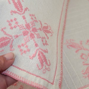 May include: Two white linen napkins with pink embroidered floral designs. The napkins have a pink border.