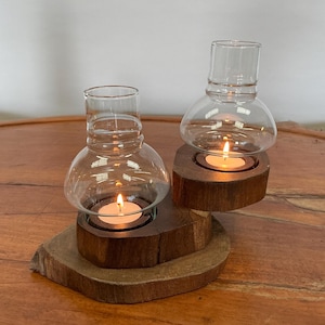 May include: A wooden candle holder with two glass candle holders. The candle holders are lit and the wood is a dark brown colour.