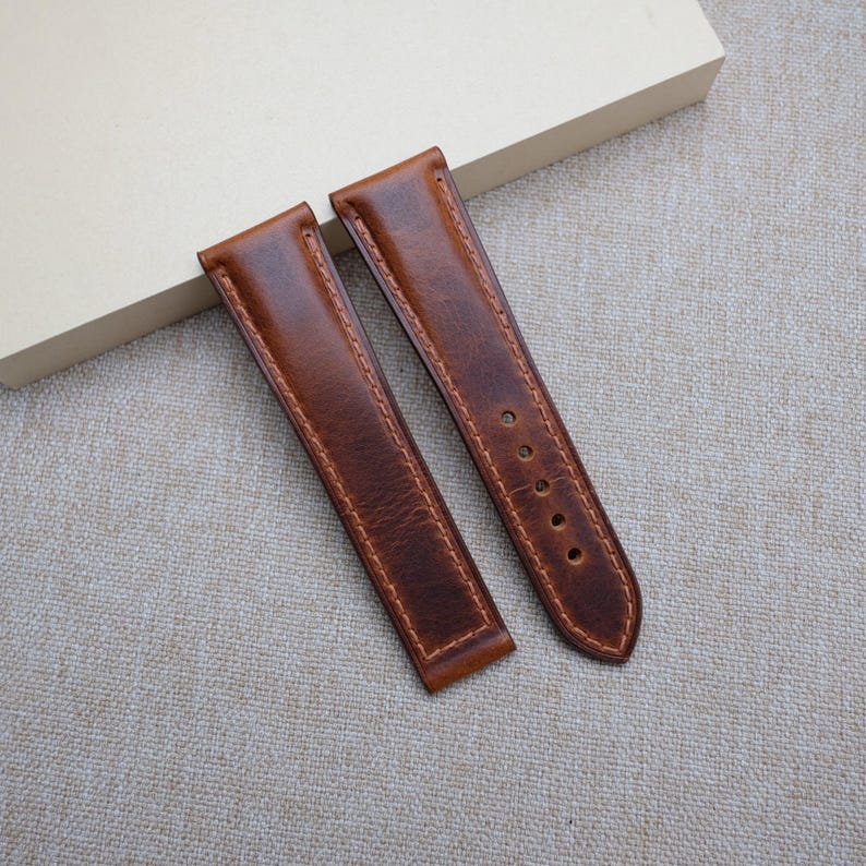 May include: Two brown leather watch straps with stitching around the edges.
