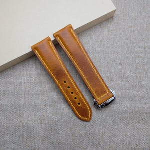 May include: Two brown leather watch straps with yellow stitching. The straps have a silver buckle.
