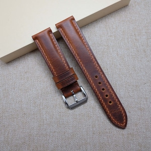 May include: Two brown leather watch straps with stitching detail. The straps have a silver buckle.