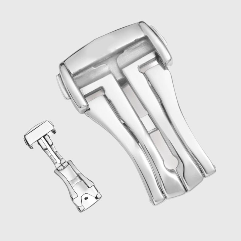 May include: A silver watch band clasp with a deployment buckle. The clasp has a polished finish and a smooth, rounded design.