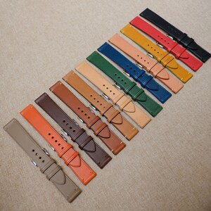 K&ouml;nnte beinhalten: Ein Set mit 12 Lederarmb&auml;ndern in verschiedenen Farben, darunter Braun, Orange, Rot, Blau, Gr&uuml;n und Beige. Die Armb&auml;nder sind in einer Reihe angeordnet, wobei die dunkelste Farbe oben und die hellste Farbe unten ist.