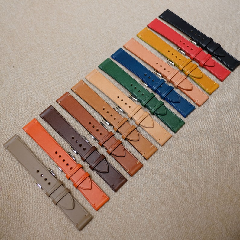K&ouml;nnte beinhalten: Ein Set mit 12 Lederarmb&auml;ndern in verschiedenen Farben, darunter Braun, Orange, Rot, Blau, Gr&uuml;n und Beige. Die Armb&auml;nder sind in einer Reihe angeordnet, wobei die dunkelste Farbe oben und die hellste Farbe unten ist.