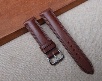 May include: Two brown leather watch straps with silver buckles. The straps are on a light brown fabric surface.