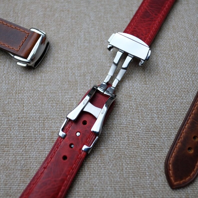 May include: A red leather watch strap with a silver buckle. The strap is attached to a silver clasp.