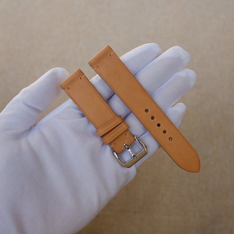 K&ouml;nnte beinhalten: Zwei braune Lederarmb&auml;nder mit silbernen Schlie&szlig;en. Die Armb&auml;nder liegen auf einer wei&szlig;en Oberfl&auml;che.