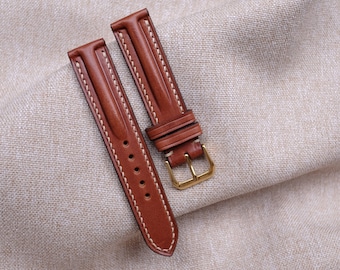Könnte beinhalten: Zwei braune Lederarmbänder mit weißen Nähten. Die Armbänder haben goldene Schließen.