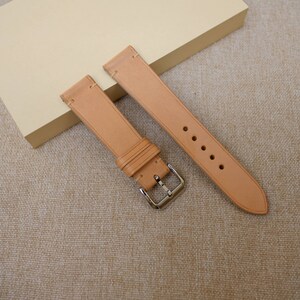 K&ouml;nnte beinhalten: Zwei hellbraune Lederarmb&auml;nder mit silbernen Schlie&szlig;en. Die Armb&auml;nder liegen auf einer beigefarbenen Stoffoberfl&auml;che.