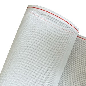 Può includere: Un rotolo di tessuto a rete bianco con un bordo cucito rosso. Il tessuto è tessuto in un motivo a griglia fine.