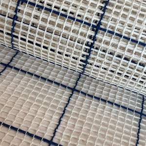 May include: A stiff, off-white rug hooking canvas featuring a grid pattern formed by dark navy blue lines. The fabric has a distinct open-weave structure with evenly spaced square holes, designed for needlepoint, latch hook, or embroidery projects.