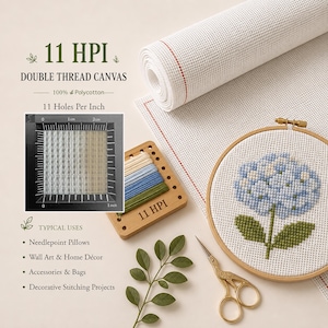 May include: A roll of white 11 HPI double thread polycotton canvas, a wooden embroidery hoop containing a blue hydrangea cross-stitch pattern, a wooden thread organizer with colored embroidery floss, and gold-toned metal scissors.
