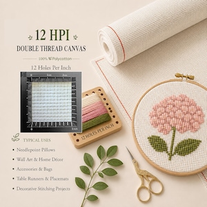 May include: A roll of off-white 12 HPI double thread polycotton canvas with a red guide line, a wooden embroidery hoop containing a pink hydrangea cross-stitch, a wooden thread organizer with colored floss, and gold stork embroidery scissors.