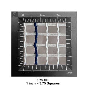 May include: A white needlepoint canvas mesh with a single vertical dark blue thread, positioned against a black frame with a ruler showing 1 inch equals 3.75 squares, labeled 3.75 HPI, indicating a density of 3.75 holes per inch for embroidery.