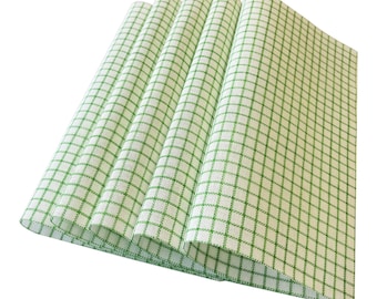 May include: A stack of four folded white and green checkered placemats. The placemats have a grid pattern of green lines on a white background. The edges of the placemats are visible, showing the layered folds.