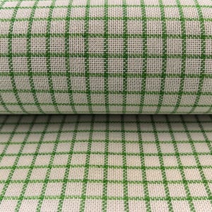 Puede incluir: Primer plano de un rollo de tela con un diseño a cuadros verdes y crema. La tela tiene una textura tejida, con líneas verdes que forman una cuadrícula sobre el fondo crema. La tela está doblada, mostrando el patrón en dos capas.