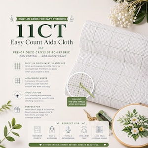May include: A roll of white 11CT Easy Count Aida cloth featuring a pre-printed grid pattern for cross-stitch projects. The fabric is 100% cotton with a block weave. A wooden embroidery hoop displays a finished floral design with white daisies.