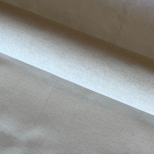Puede incluir: Primer plano de una tela de lona blanca enrollada. La tela tiene un tejido fino y una textura suave.