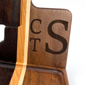 May include: A wooden valet tray with a dark brown, light brown, and white wood grain pattern. The tray has a small compartment and two slots for holding items. The initials "CT S" are engraved on the side of the tray.