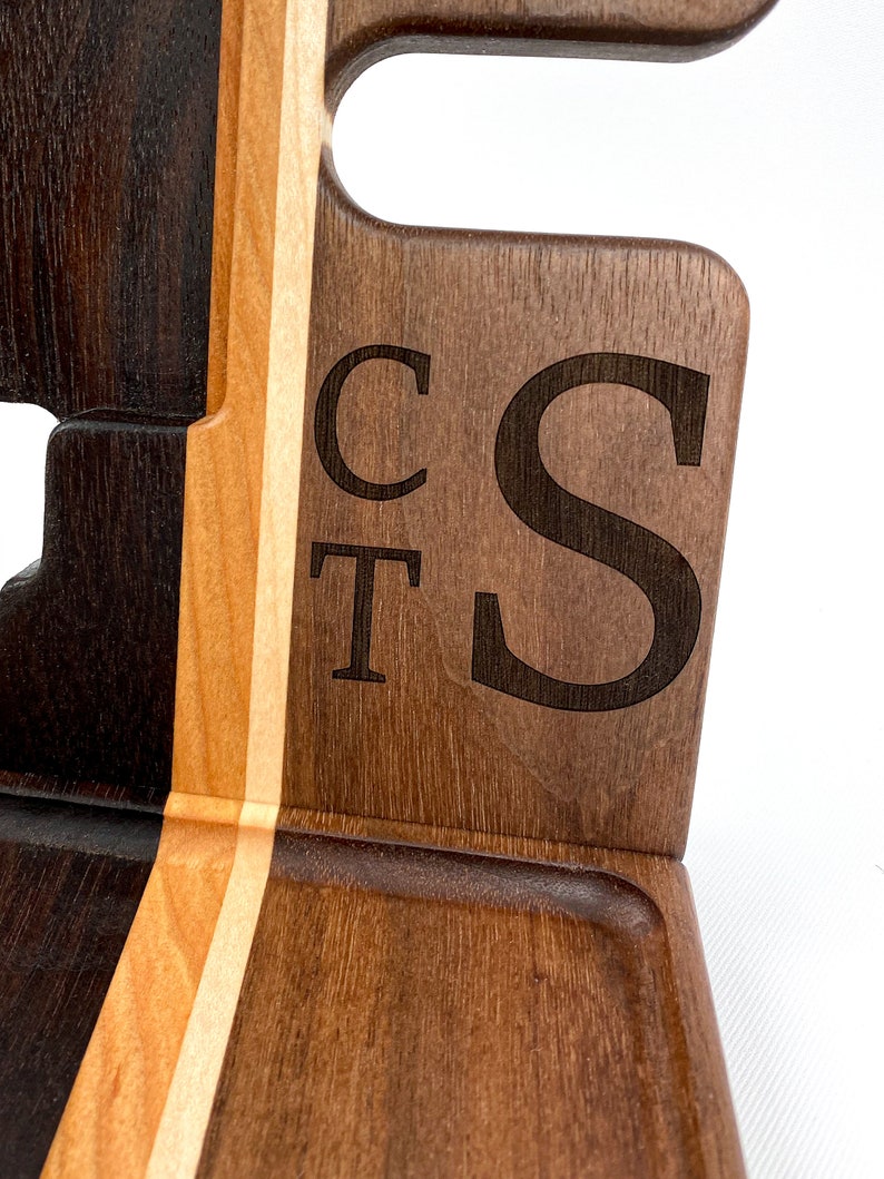 May include: A wooden valet tray with a dark brown, light brown, and white wood grain pattern. The tray has a small compartment and two slots for holding items. The initials "CT S" are engraved on the side of the tray.