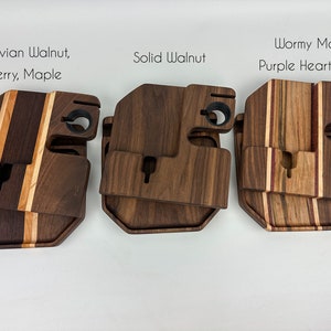 May include: Three wooden phone stands with different wood types. The first stand is made of Peruvian walnut, cherry, and maple. The second stand is made of solid walnut. The third stand is made of wormy maple, purple heart, and maple.