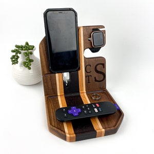 May include: A wooden phone and watch stand with a charging station for a phone. The stand has a tray for a remote control and a ring. The stand is personalized with the initials "C.T.S."