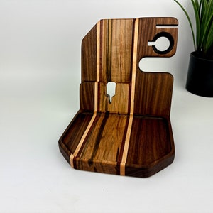 May include: A wooden phone stand with a tray and a phone holder. The stand is made of walnut and maple wood and has a striped pattern.