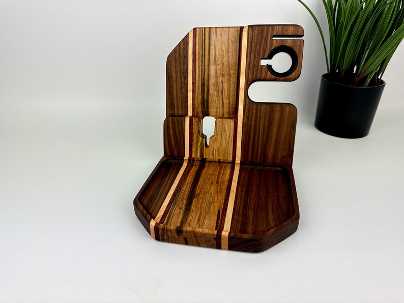 May include: A wooden phone stand with a tray and a phone holder. The stand is made of walnut and maple wood and has a striped pattern.