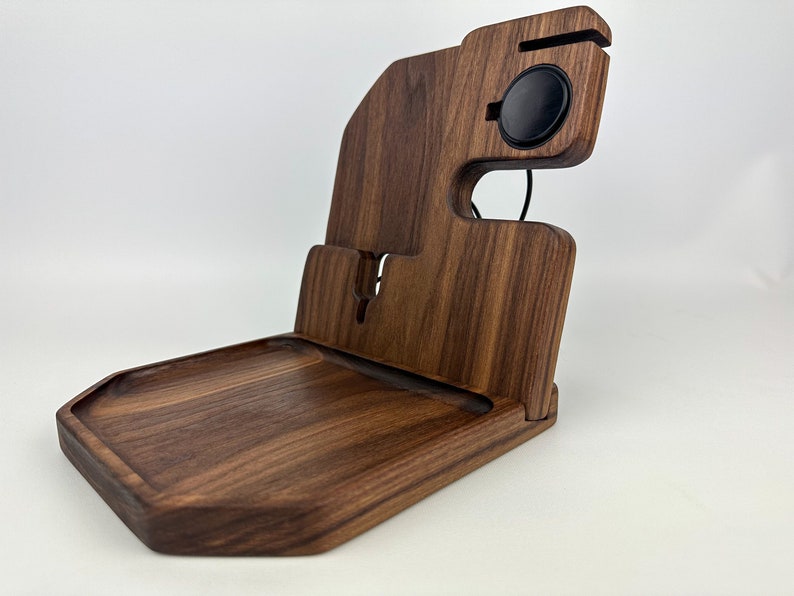 May include: A wooden charging station with a tray, a phone stand, and a wireless charging pad for a smartwatch. The station is made of dark brown walnut wood.