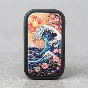 Op de afbeelding: Een rechthoekig telefoonhoesje met een levendige illustratie in glas-in-loodstijl van een grote blauwe oceaangolf, een verre bergtop, een heldere gele zon en roze kersenbloesemtakken, geplaatst in een donker, gestructureerd frame.