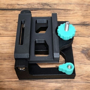 May include: A black 3D printed camera mount with two teal knobs. The mount has a slot for a camera plate and a screw for attaching to a tripod.