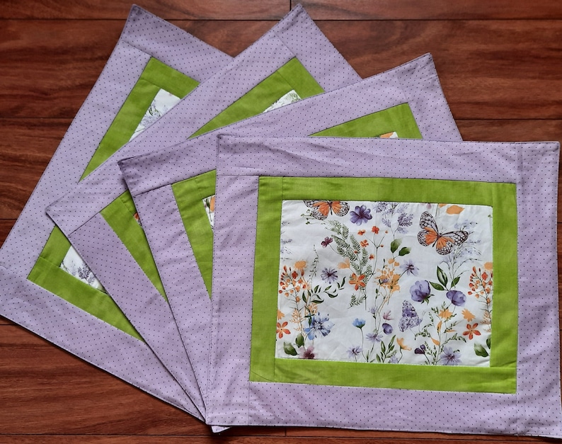 May include: Set of four purple and green placemats with a floral and butterfly design. The placemats have a white background with green borders and a floral pattern with butterflies.