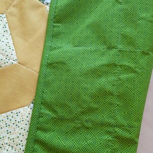 May include: A quilted fabric piece featuring a bright green section with a repeating dark green diamond pattern, adjacent to a yellow section and a white section with a small green dot pattern and a lemon print design with green leaves.