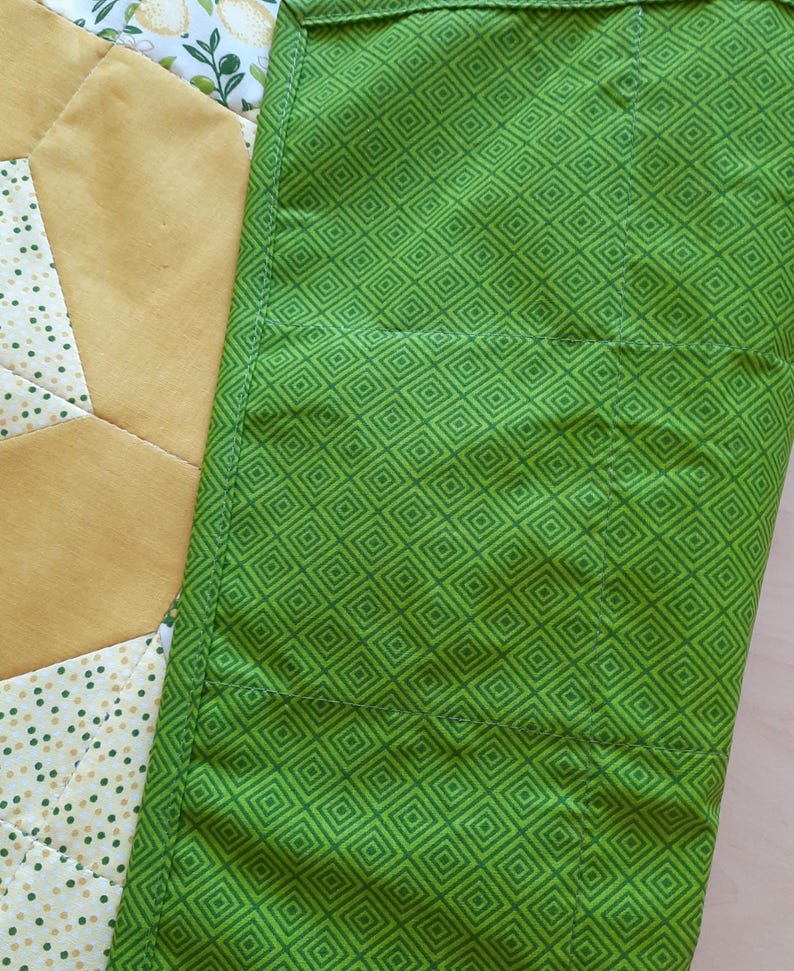May include: A quilted fabric piece featuring a bright green section with a repeating dark green diamond pattern, adjacent to a yellow section and a white section with a small green dot pattern and a lemon print design with green leaves.