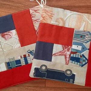 Könnte beinhalten: Zwei rote und blaue Patchwork-Topflappen mit Strandmotiv. Ein Topflappen zeigt ein Strandhaus, einen Seestern und einen blauen Van. Der andere Topflappen zeigt eine Muschel, ein Netz und den Text "California * The Great Waves".